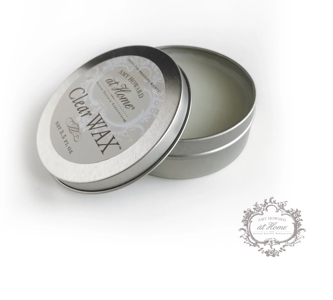 A small open tin container labeled 'Clear Wax' with a lid beside it, on a white background.