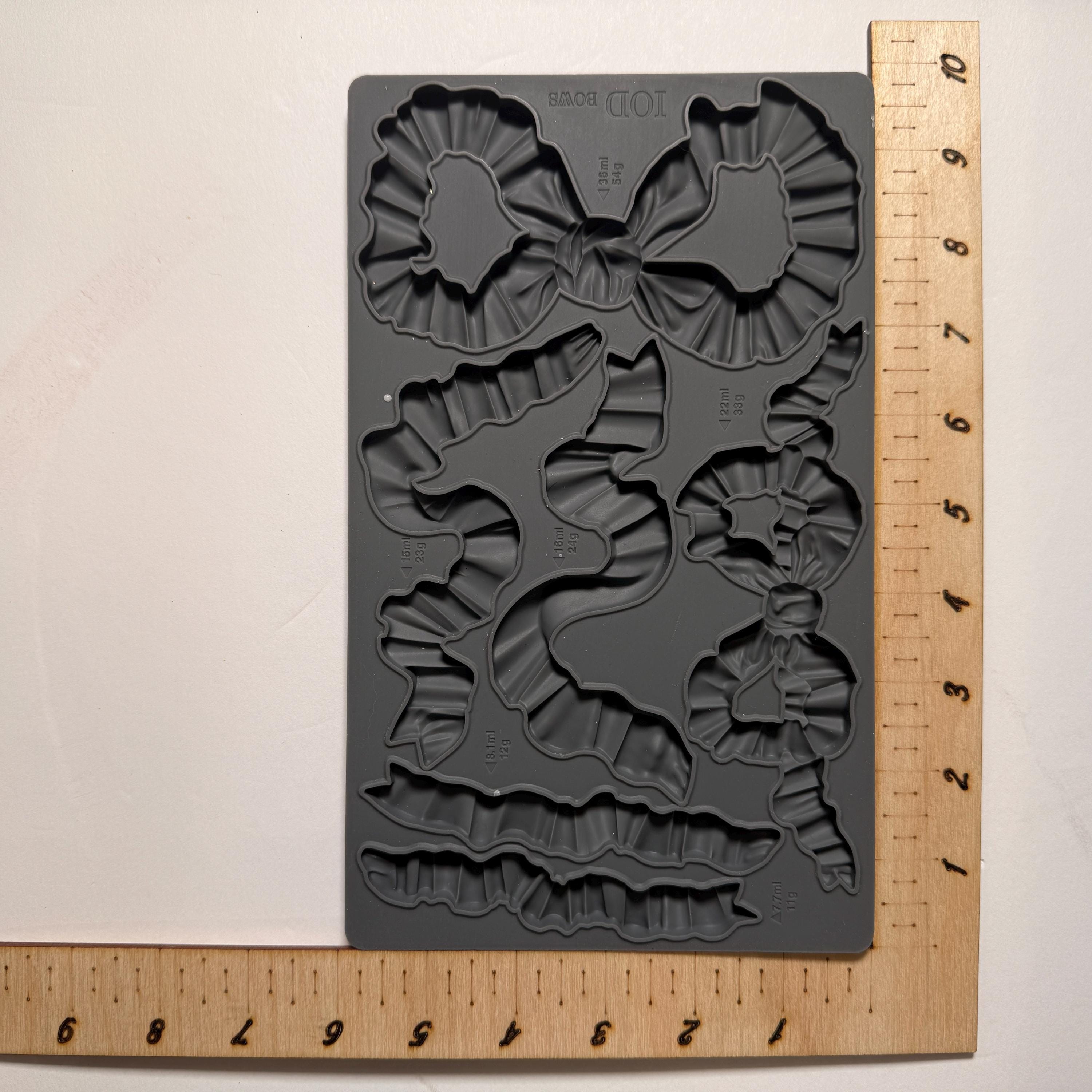 Gray silicone mold with bow shapes on a beige background with a ruler for scale.