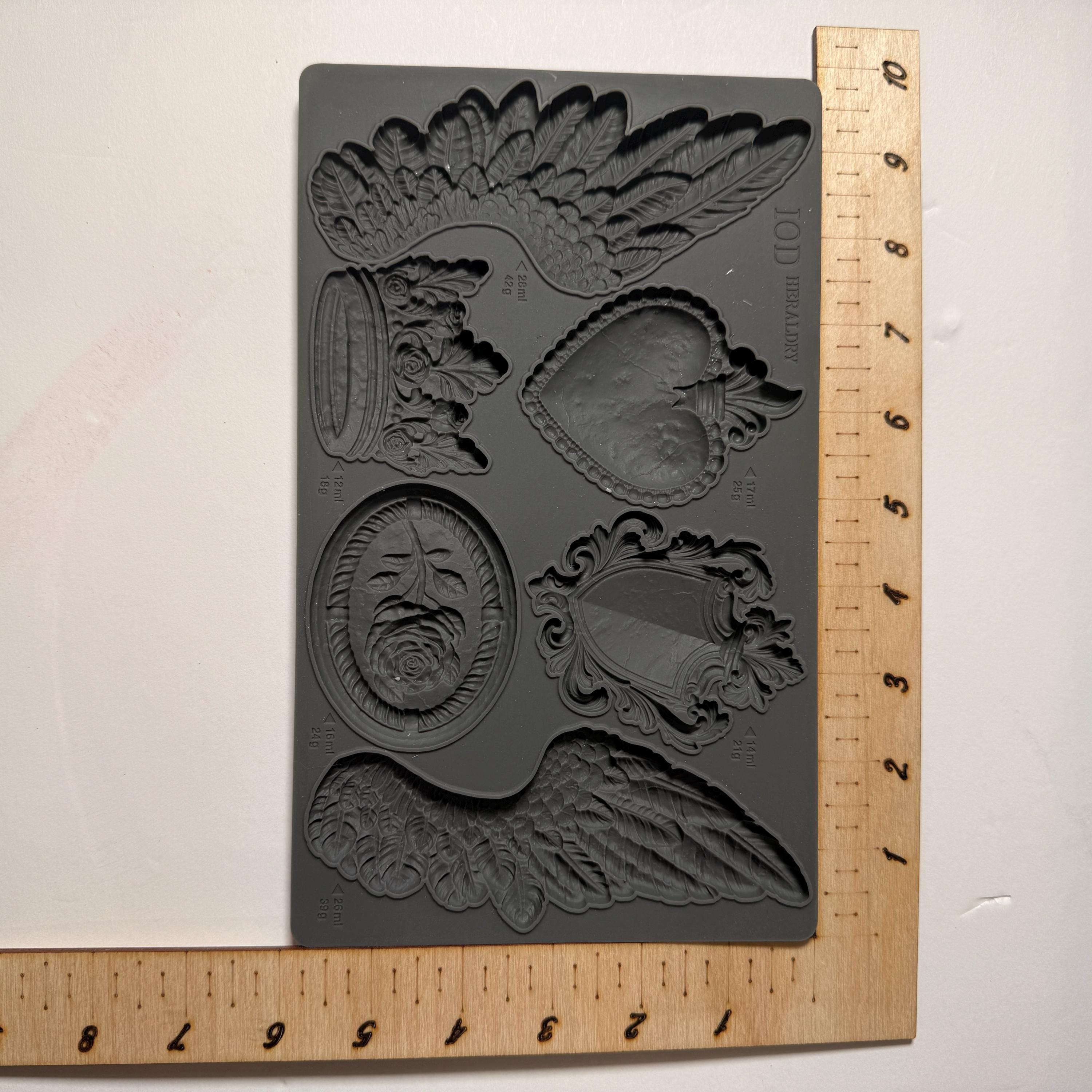 Decorative mold with winged designs on a white background with a ruler for scale.