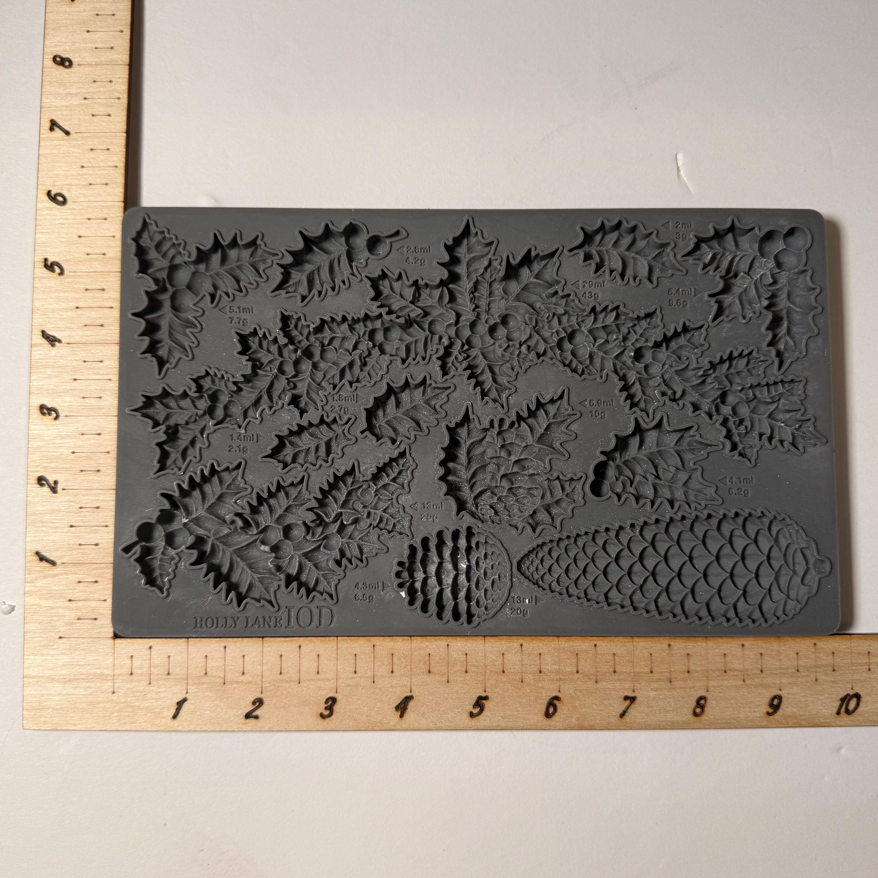 Gray silicone mold with floral and pinecone designs next to a ruler for scale.
