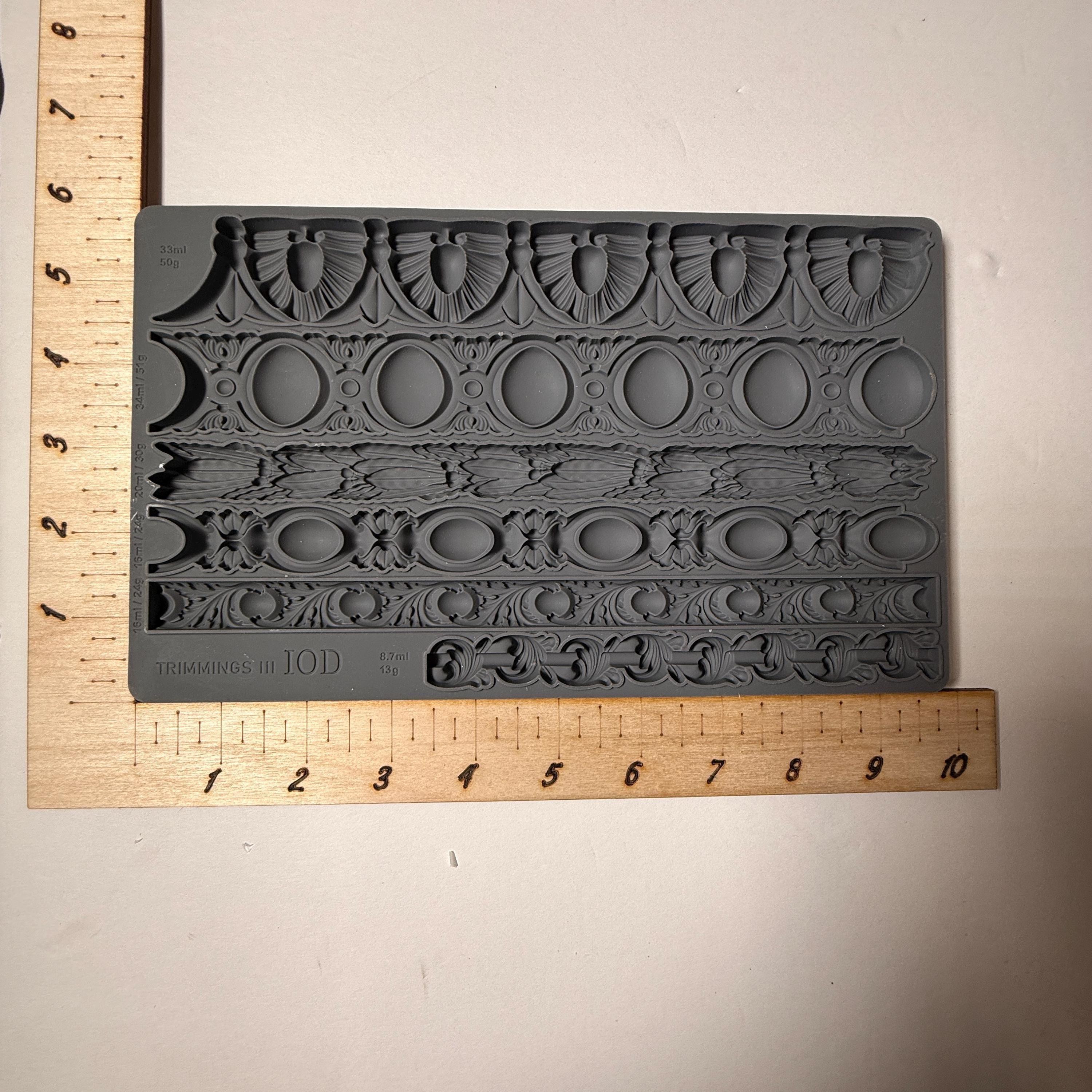 Decorative silicone mold with intricate patterns next to a wooden ruler on a beige background