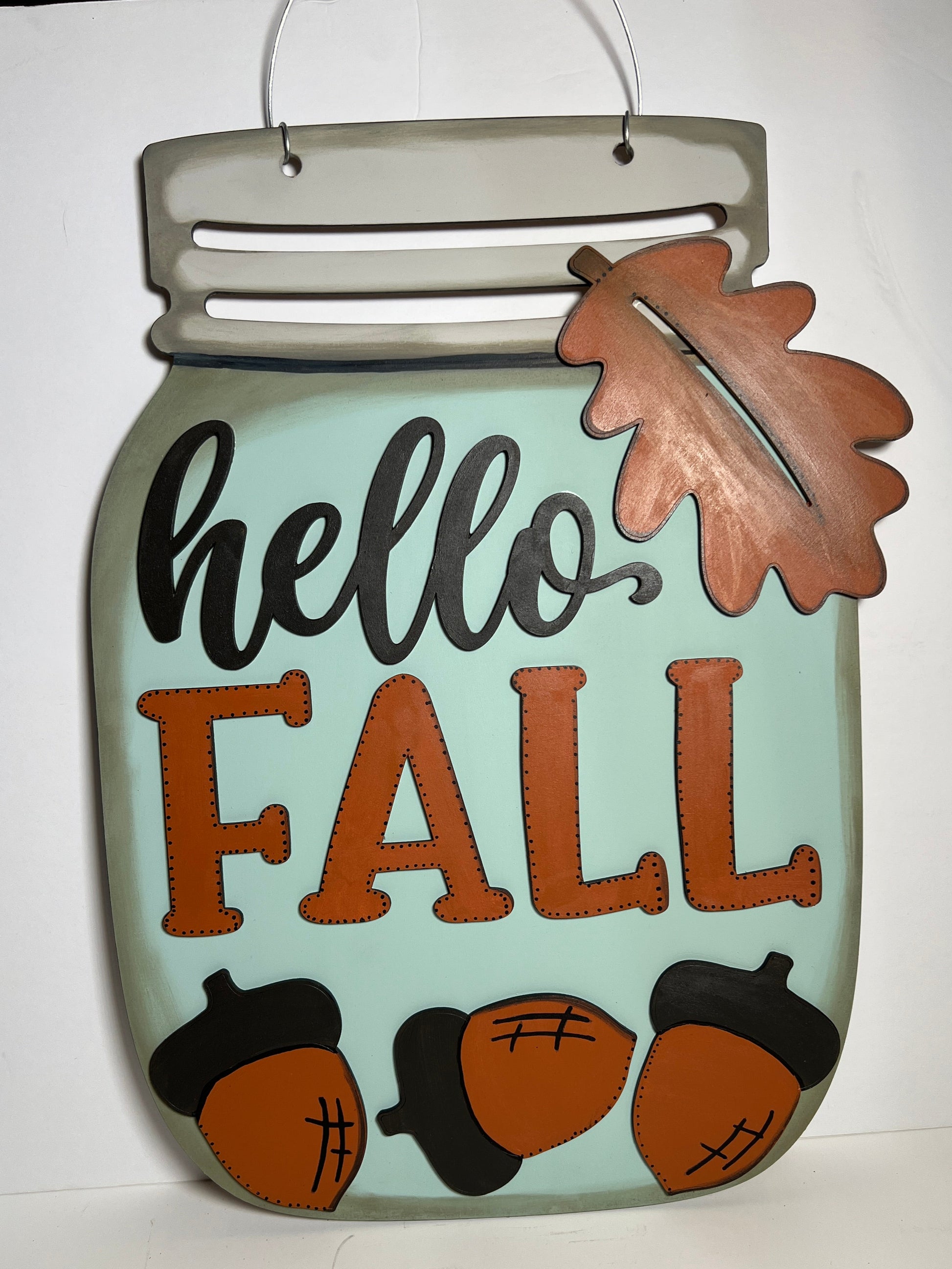Decorative sign with 'hello FALL' text and acorn designs on a light blue background.