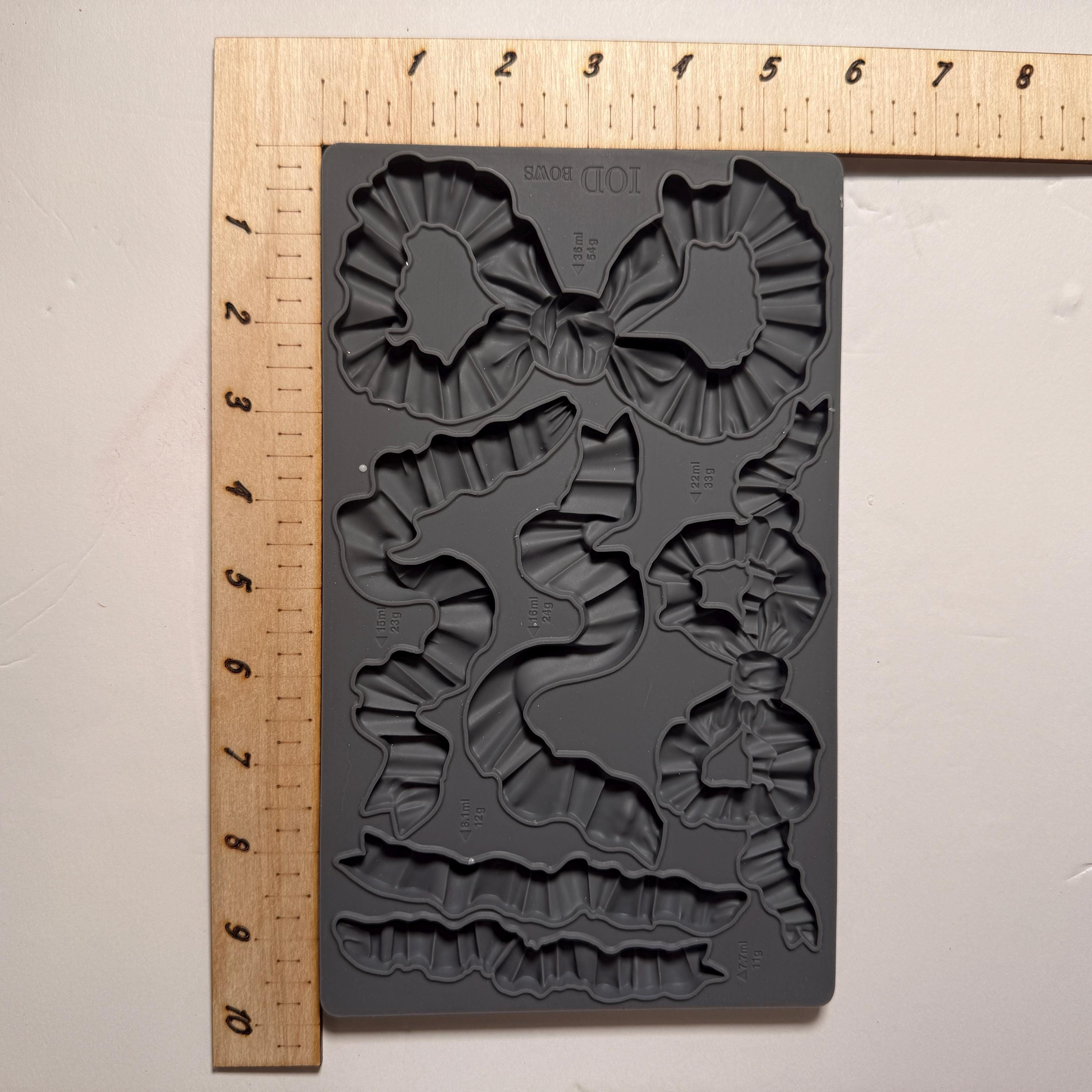 Gray silicone mold with bow and leaf designs on a white background with a ruler for scale.