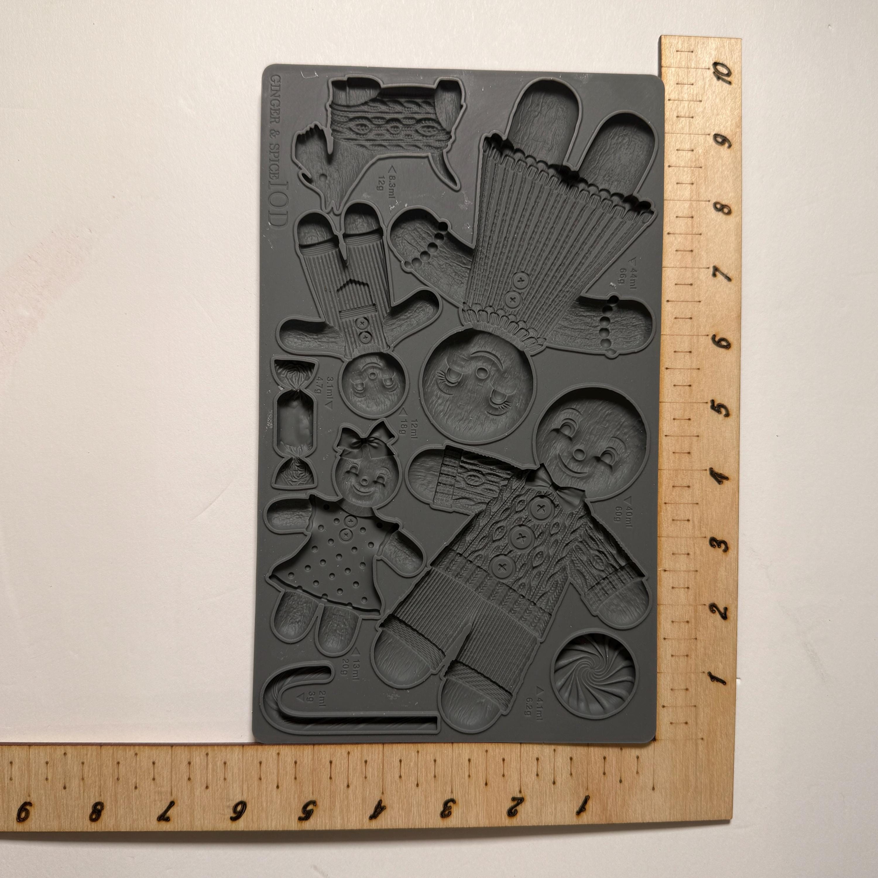 Black silicone mold with various shapes next to a wooden ruler on a beige background