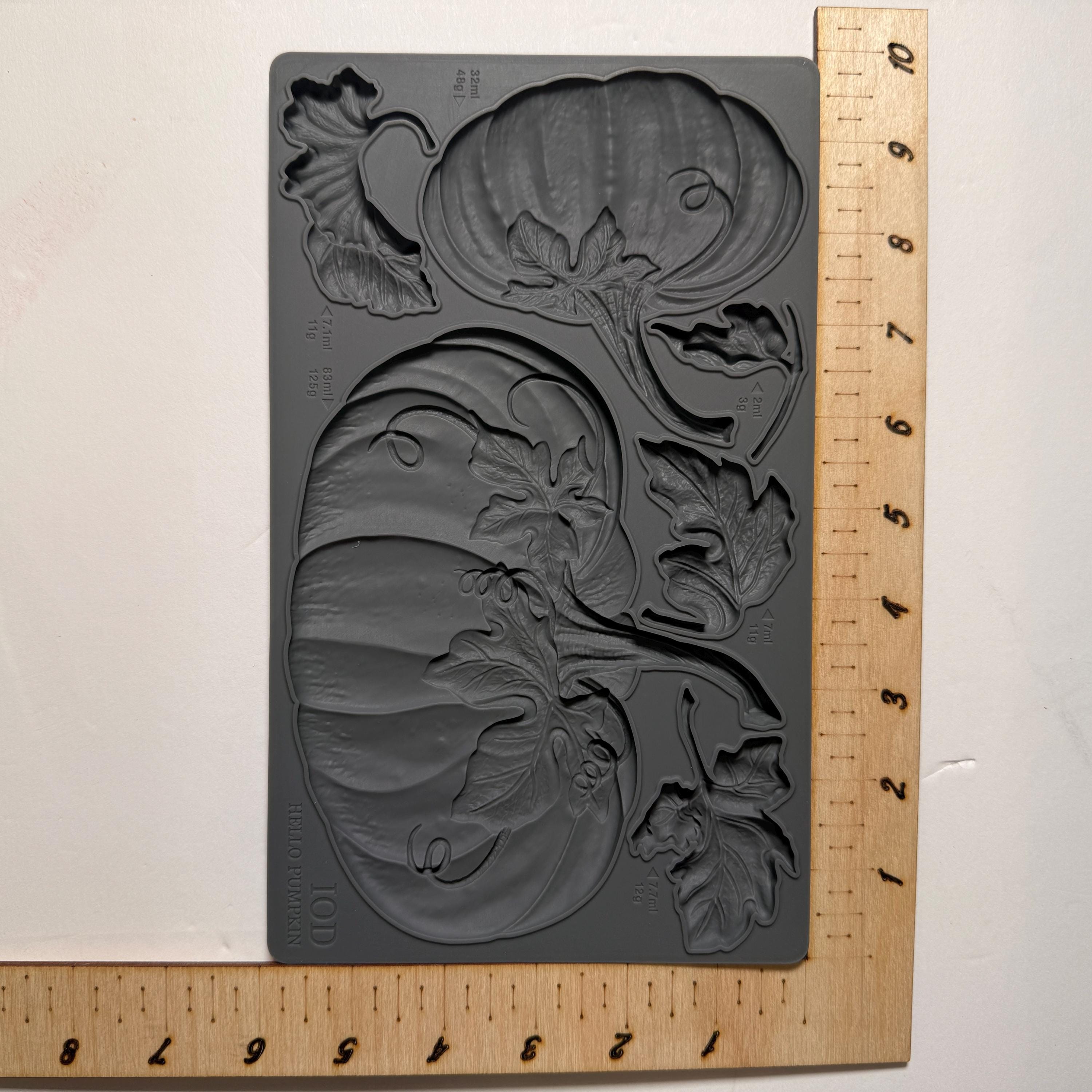 Gray silicone mold with pumpkin design on a wooden ruler for scale