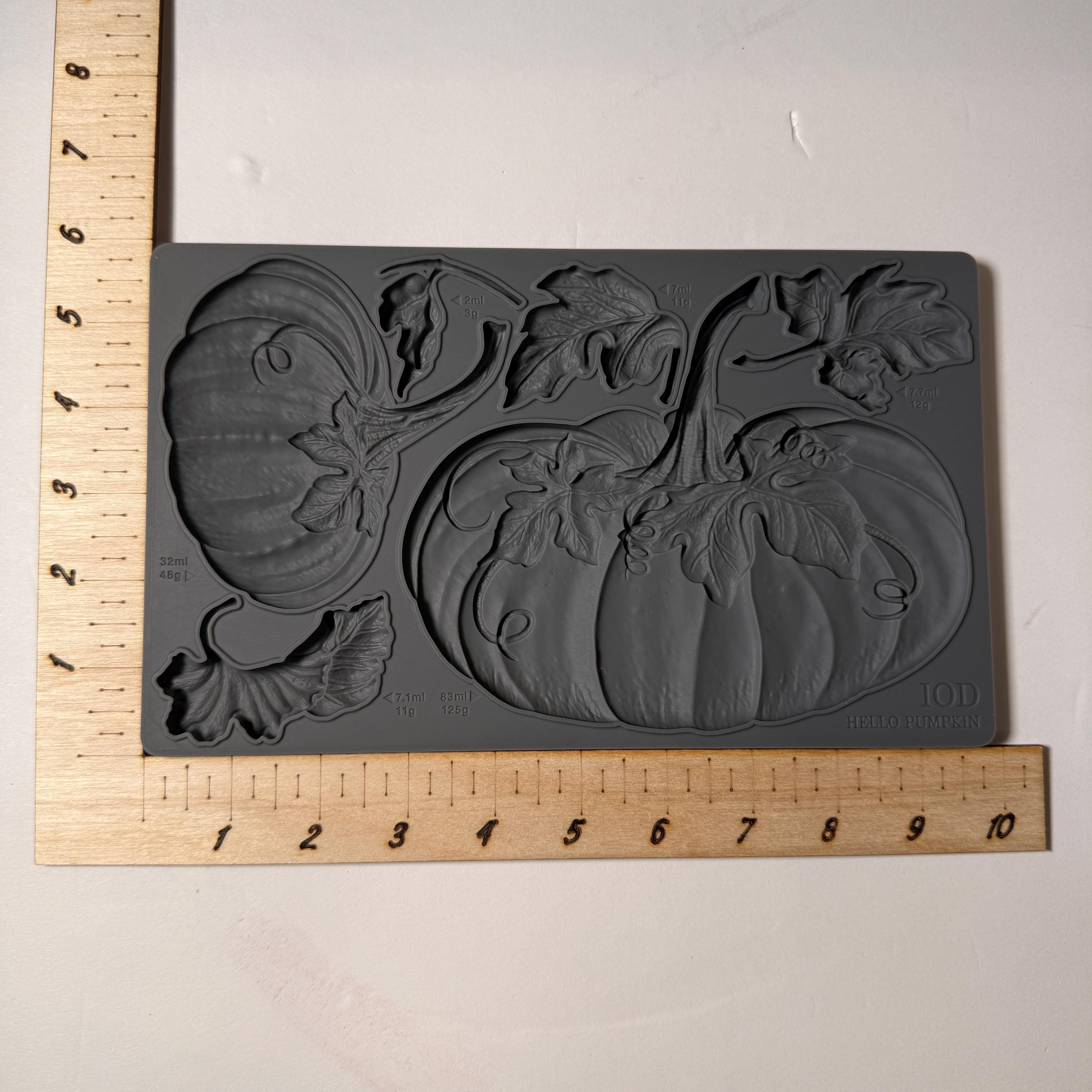 Gray silicone mold with pumpkin design on a white background, measured by a wooden ruler.