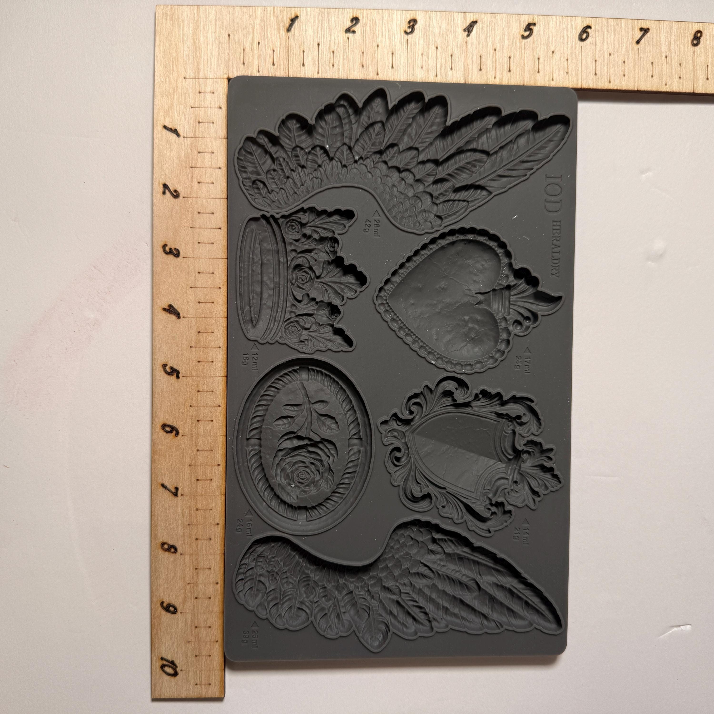 Decorative mold with intricate designs on a gray background, measured against a ruler.