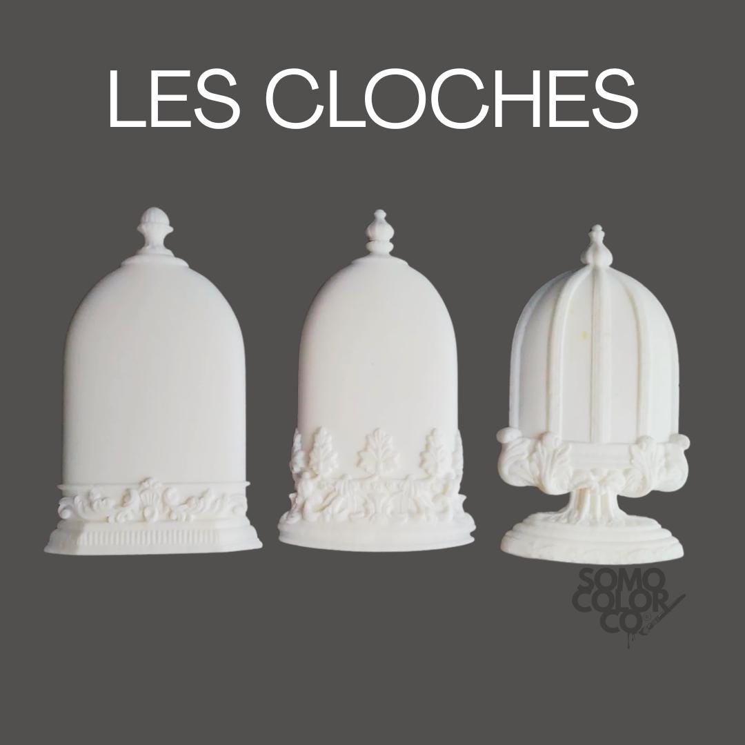 Three white decorative bell-shaped objects with intricate designs on a gray background, featuring the text 'LES CLOCHES' and 'SOMO COLOR CO'.