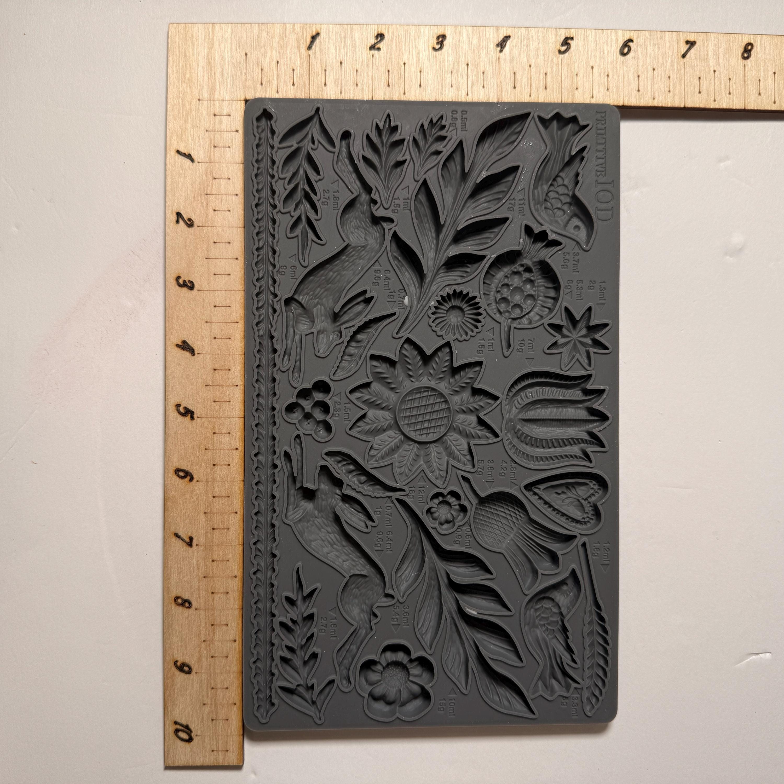 Decorative black rubber stamp with floral design next to a ruler on a light gray background