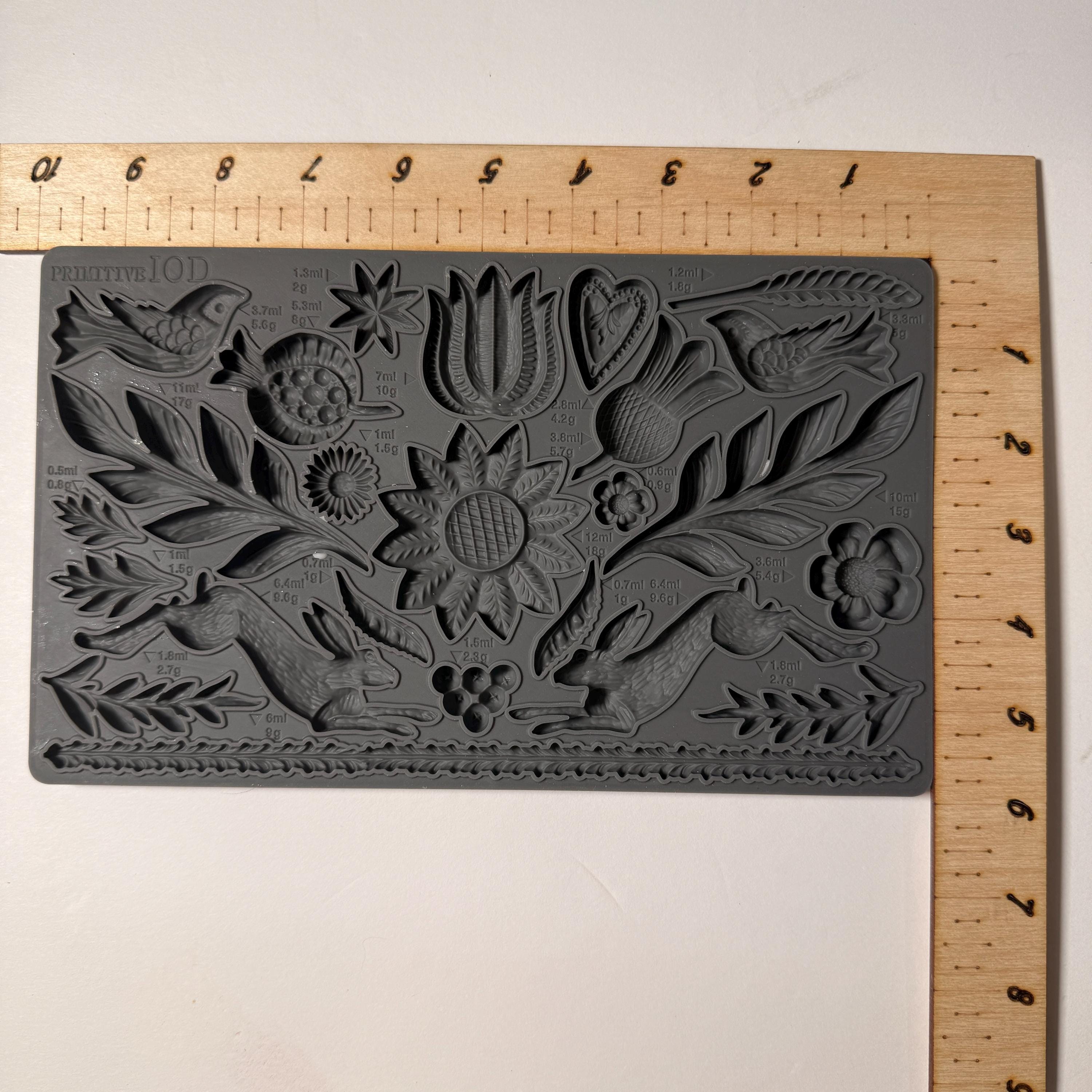 Decorative mold with floral and animal designs on a wooden board with a ruler.