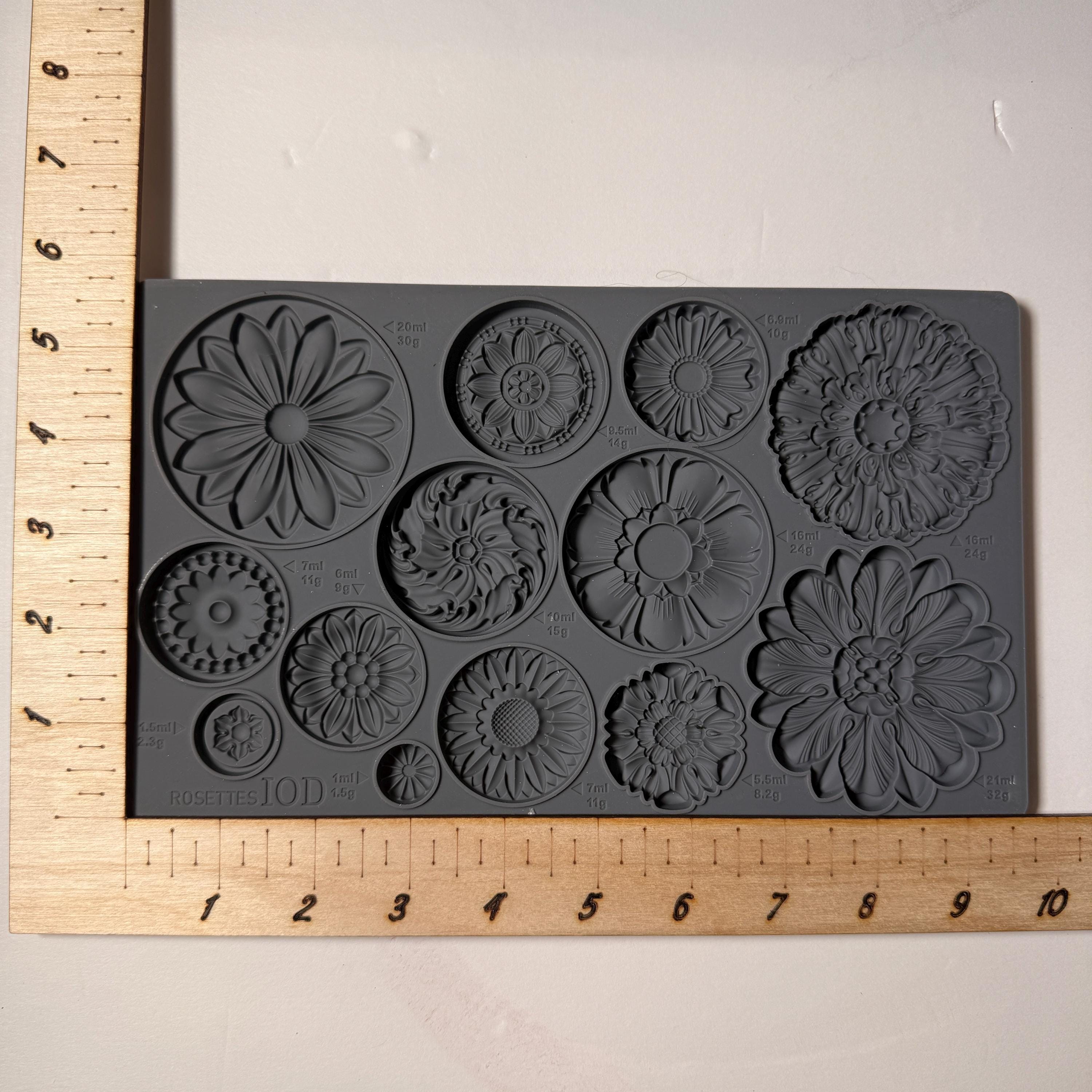 Gray silicone mold with floral designs on a white background, measured against a wooden ruler.