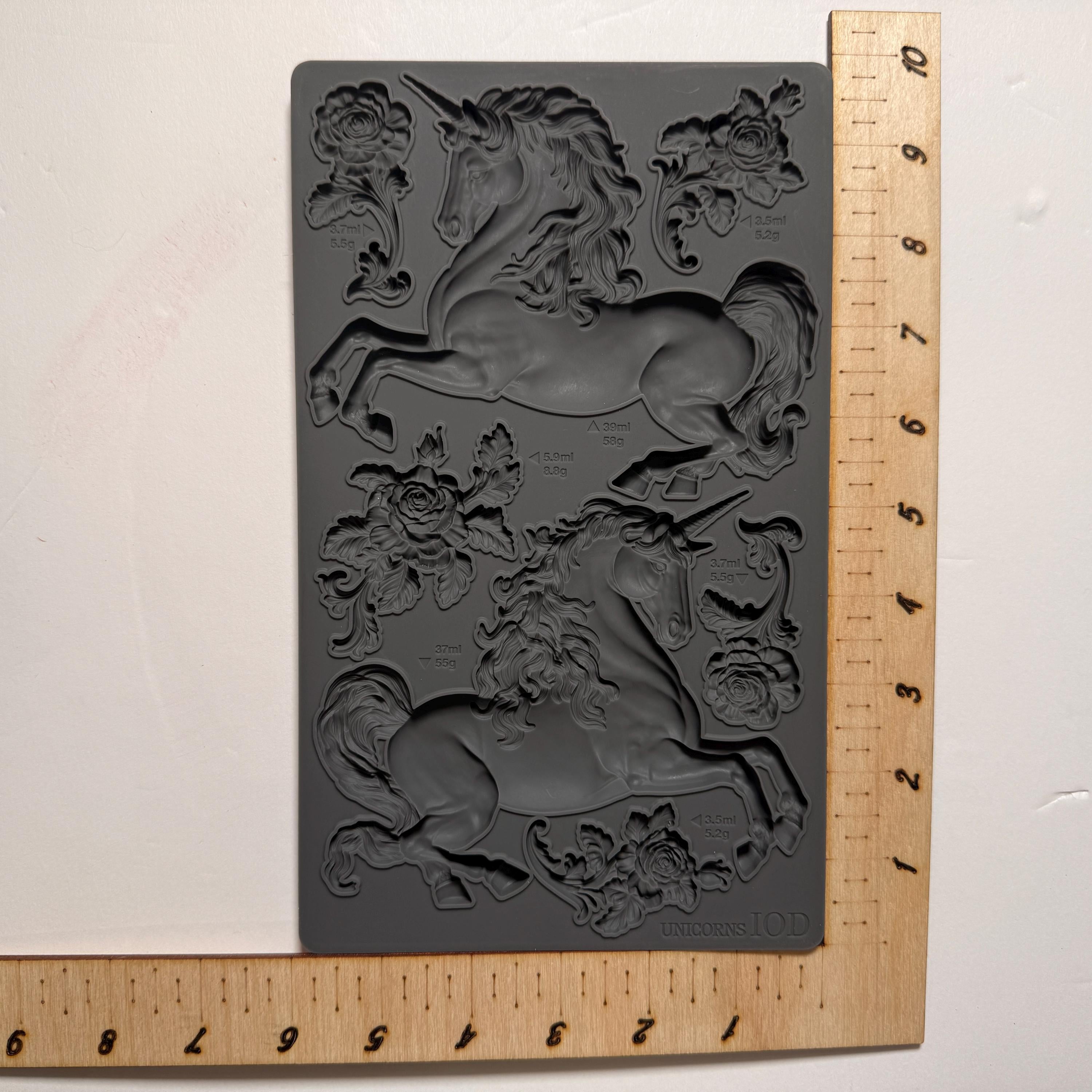 Unicorn-themed mold with floral designs on a gray background, next to a wooden ruler for scale.