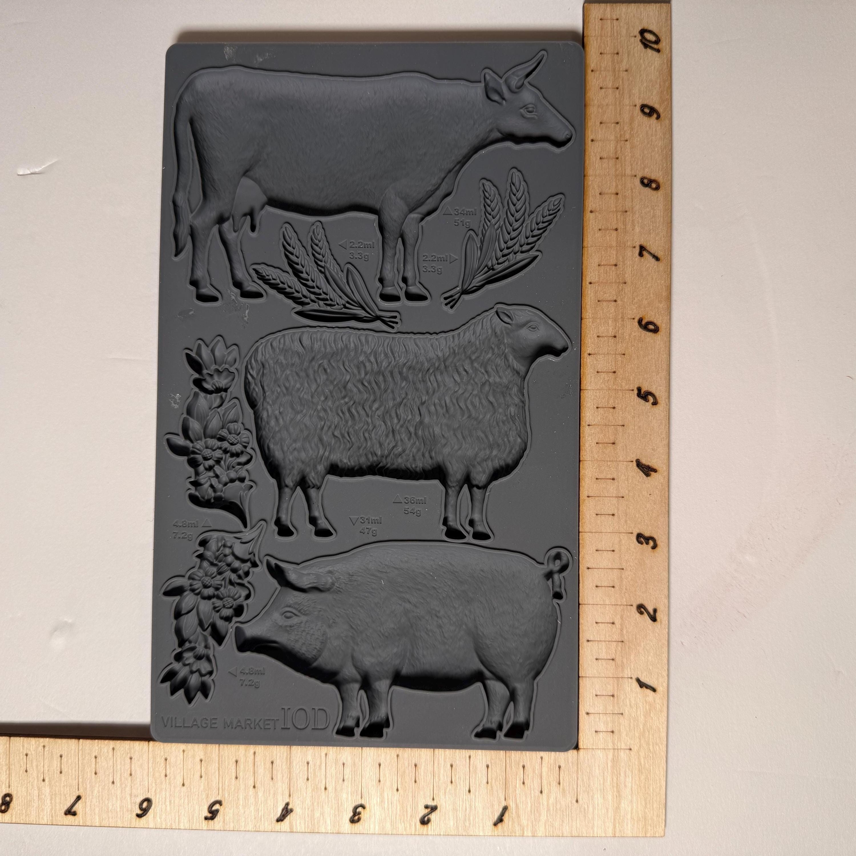 Decorative mold with cow, sheep, and pig designs on a ruler for scale.