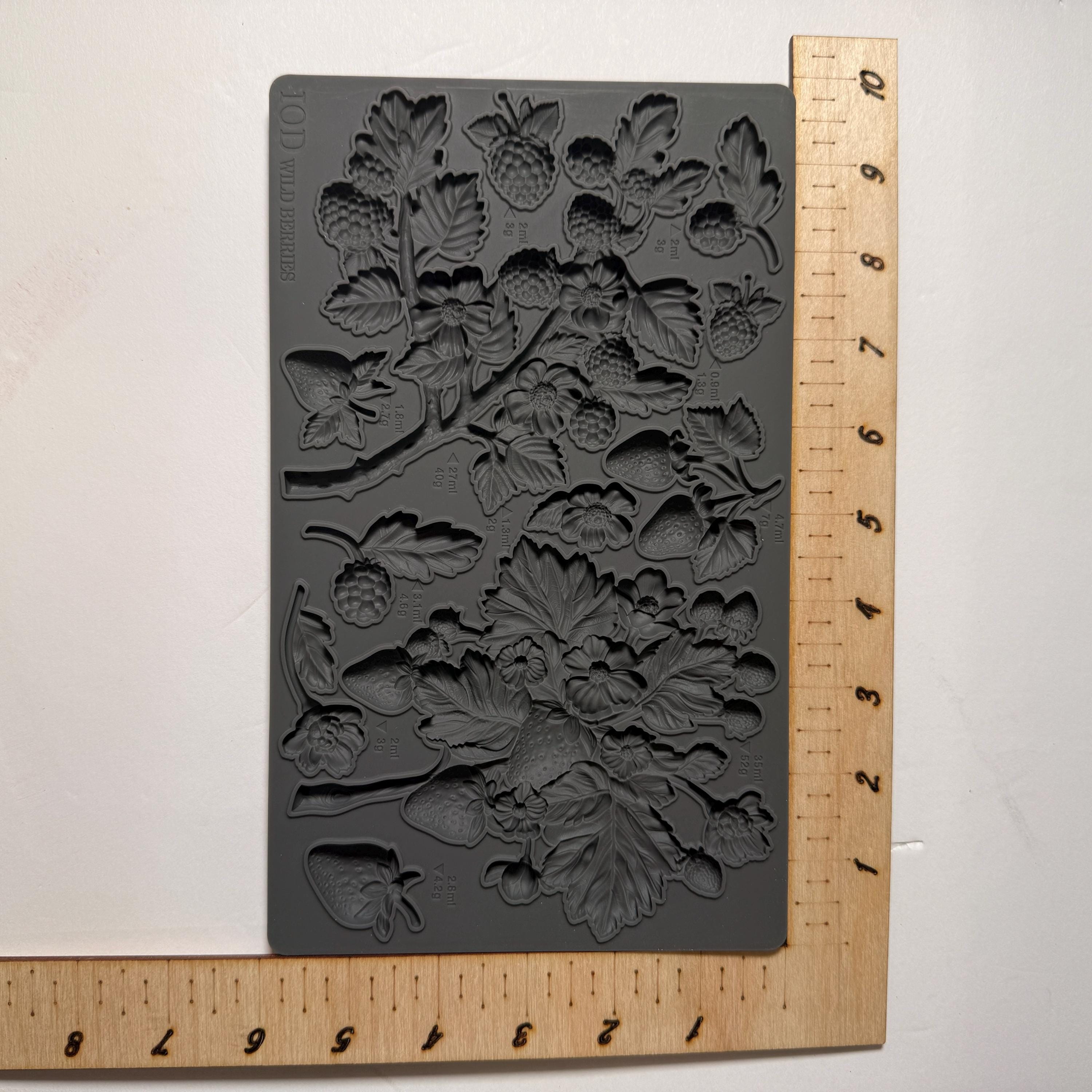 Decorative mold with floral design next to a wooden ruler for scale