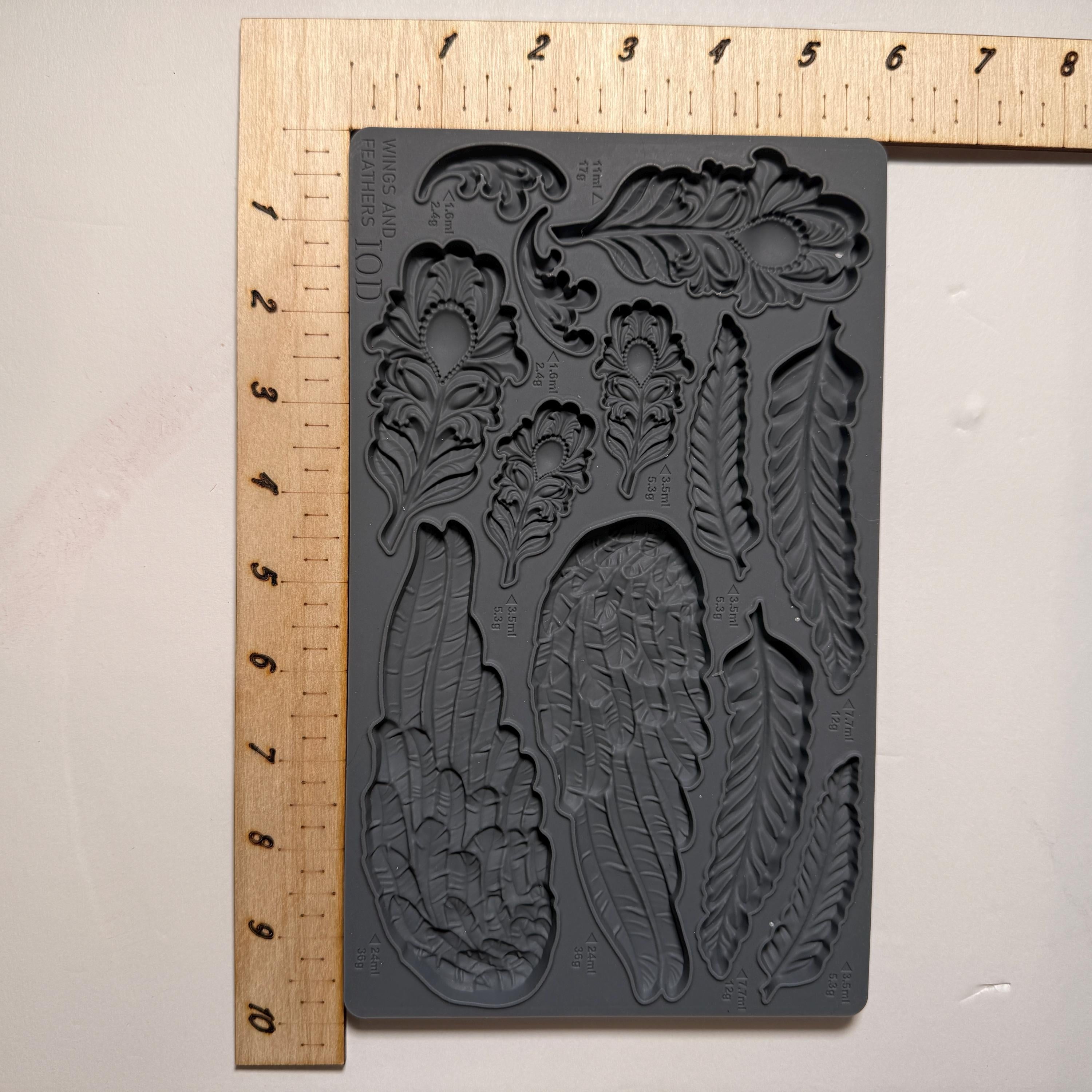 Decorative mold with floral and feather designs next to a ruler on a light background