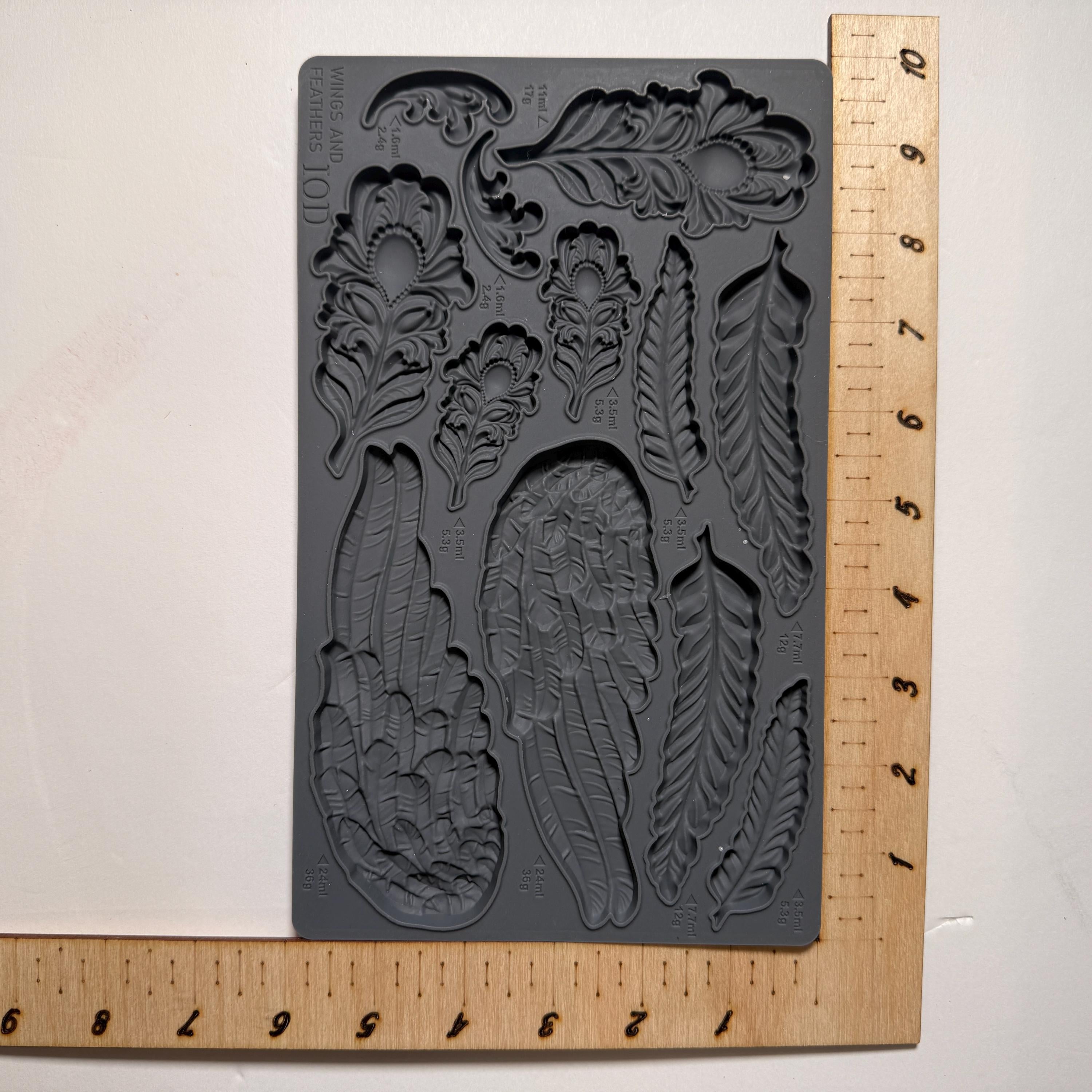 Decorative mold with feather designs next to a wooden ruler for scale.