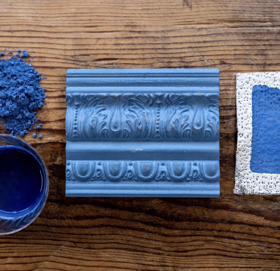 Decorative blue molding sample on a wooden surface with blue paint and a brush.